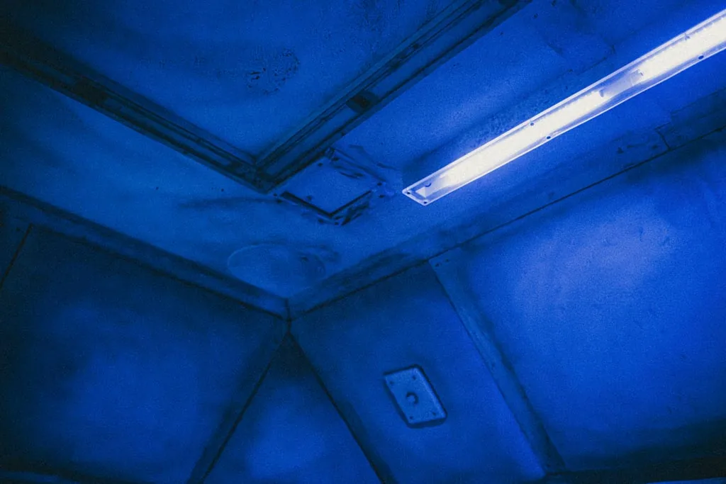 Blue light on the padded walls and bench of the Asylum cell